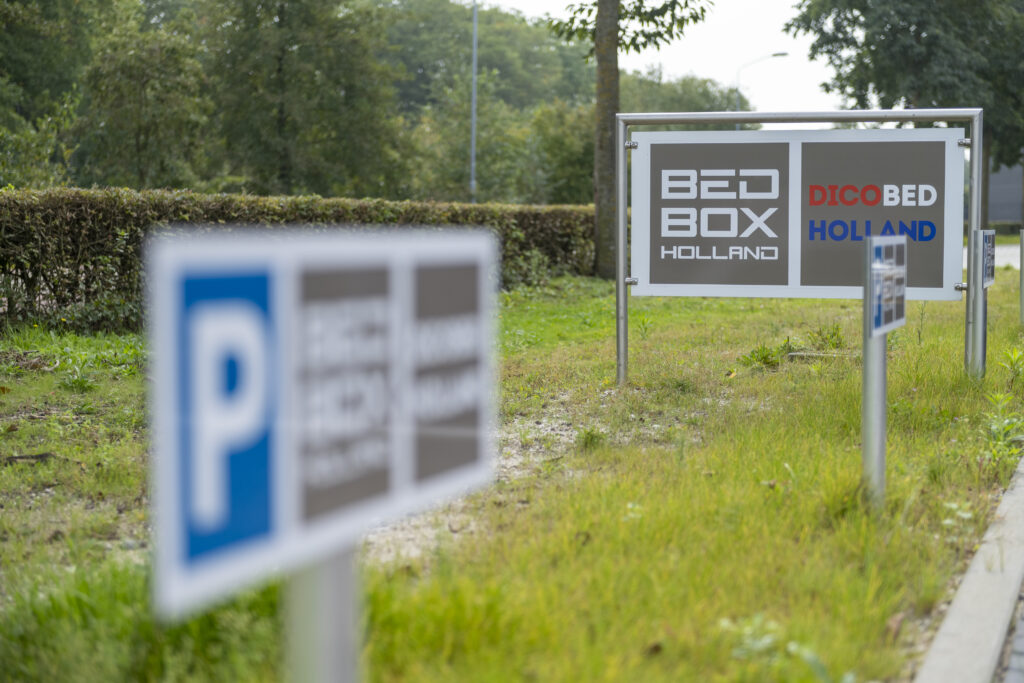 Een bord dat voor het bedrijfspand staat met het logo afgebeeld van Bedbox Holland en aangeduidt dat je kunt parkeren.